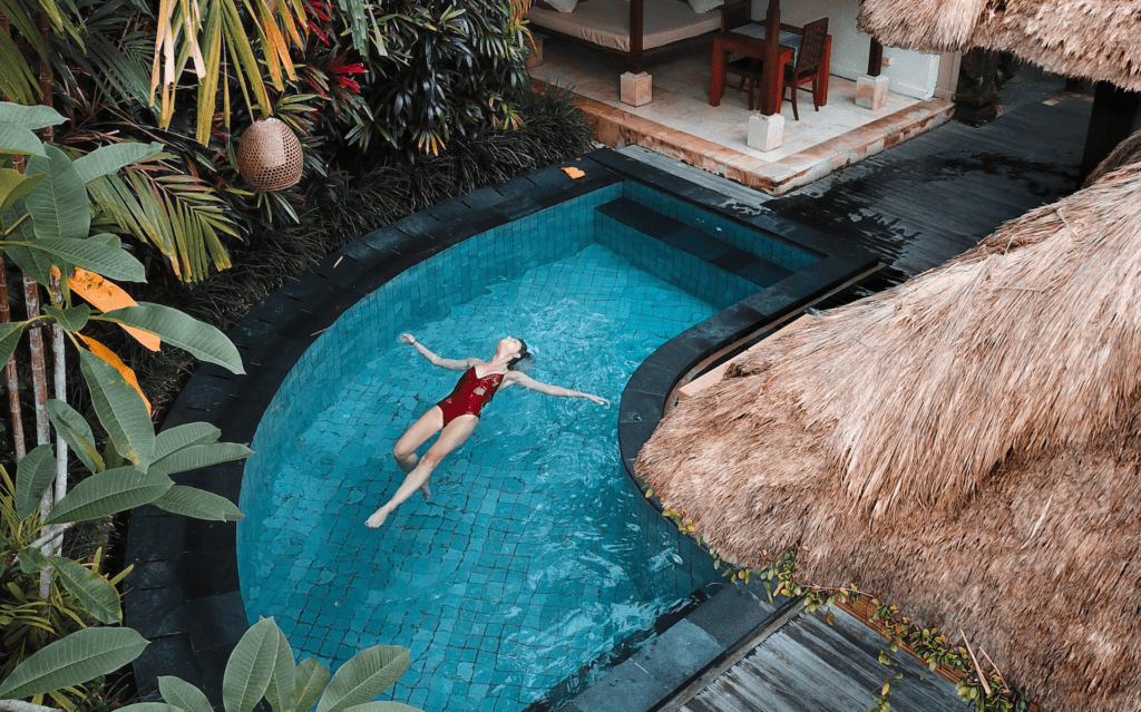 A woman relaxing in a tropical resort pool, surrounded by lush greenery and palm trees.