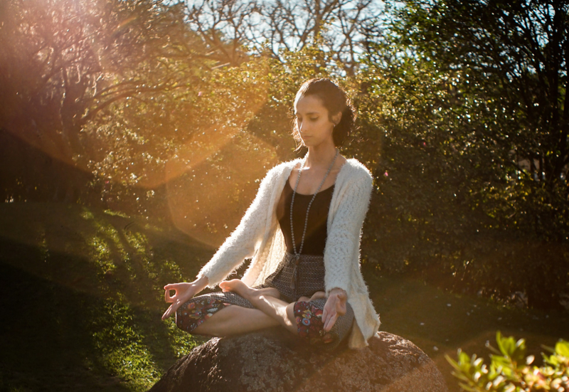 Woman meditating in a field with flowers, trees, and sunlight